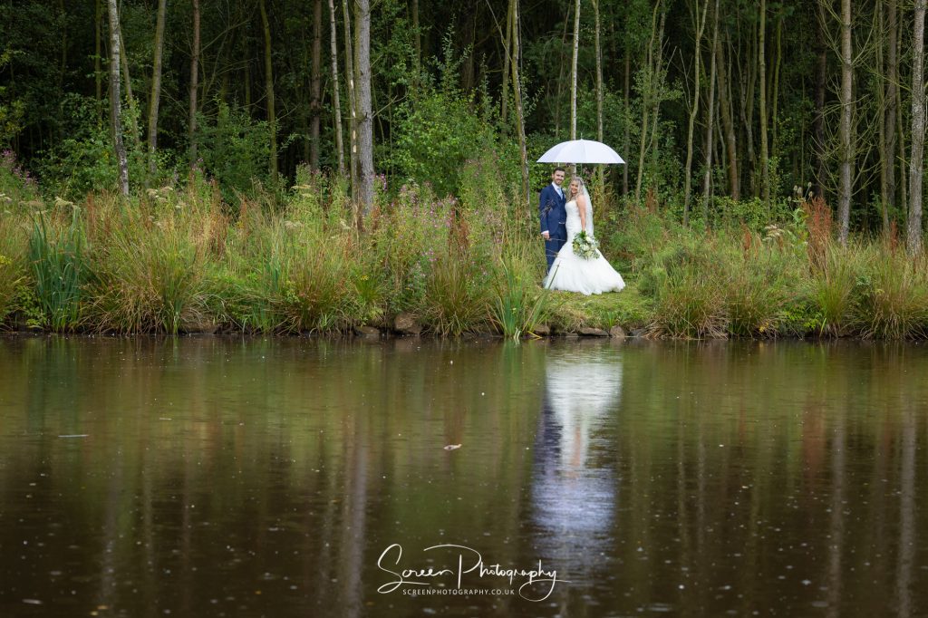 wet wedding day with lake reflection of couple with umbrella Peak District national park 