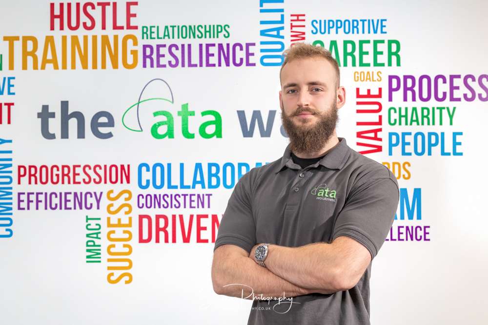 commercial photography nottingham business corporate headshot of a man with arms folded wearing a company branded t-shirt and against a wall with company missions on corporate headshots nottingham