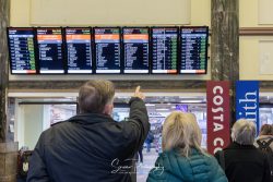 commercial photography nottingham woman and man pointing at a traing station information display board with costa coffee and wh smith signage