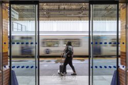 commercial photography nottingham with moving train going by and lady walking past auto closing doors on train station platform