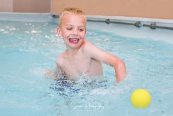 commercial photography nottingham young happy child playing and splashing with a yellow ball in a swimming pool
